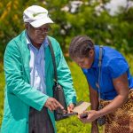 crop health advisor and farmer discussing crop pest management using a mobile tablet
